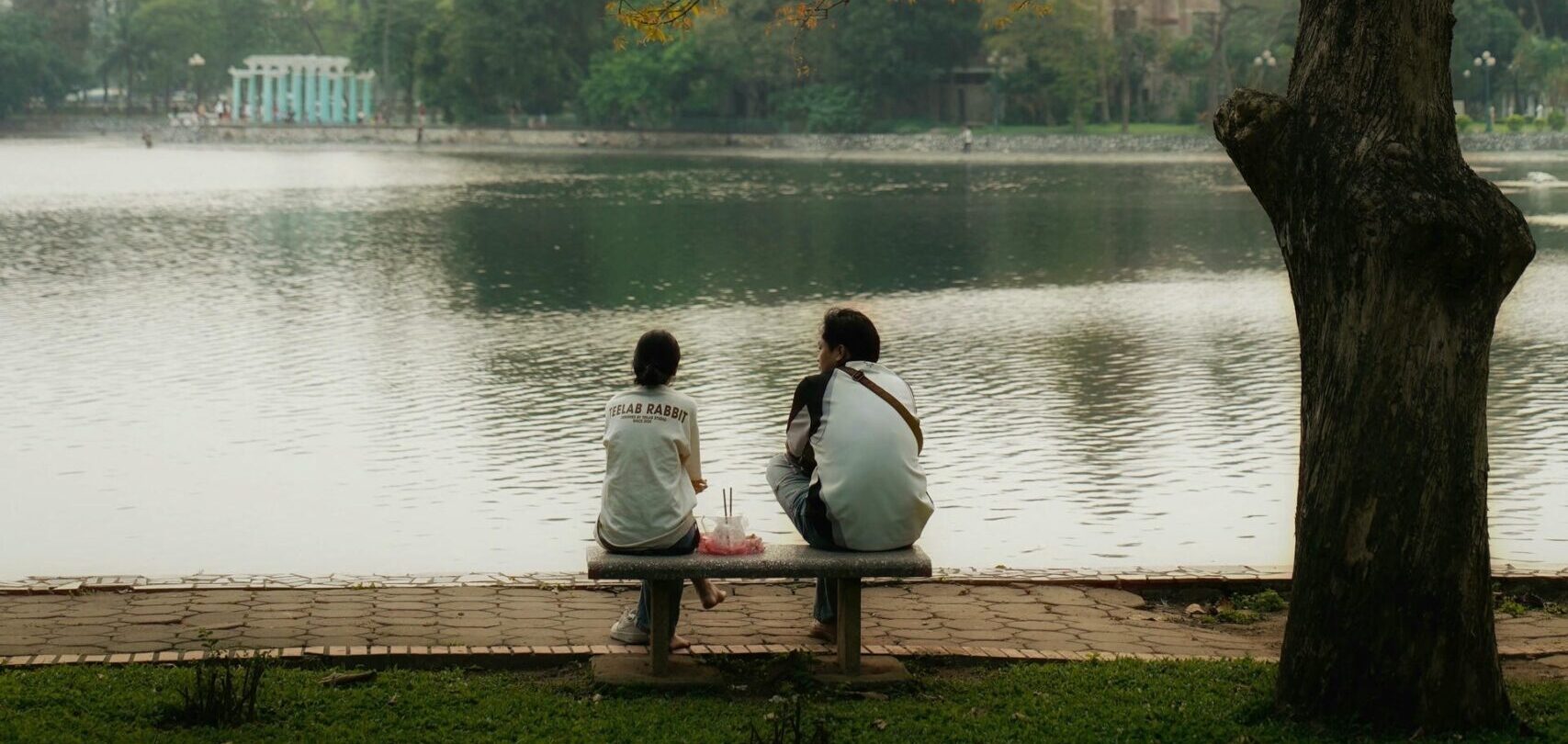 Two locals sitting by Hoan Kiem Lake at sunrise, a peaceful thing to do in Hanoi for first-time visitors