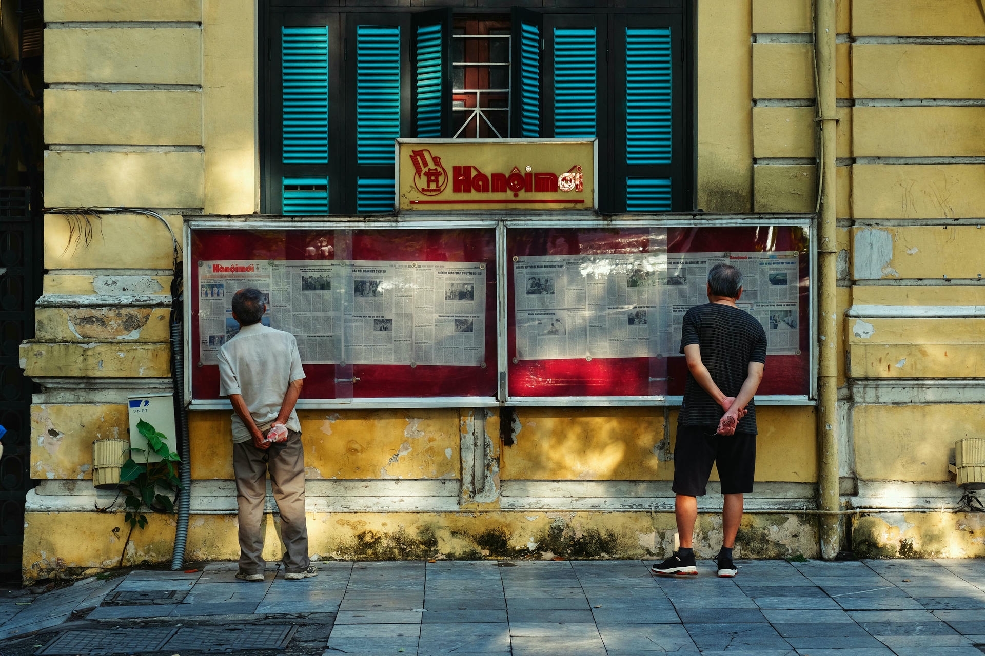 Two elderly men reading the Hanoi Mới public newspaper board, a daily local habit and cultural thing to do in Hanoi