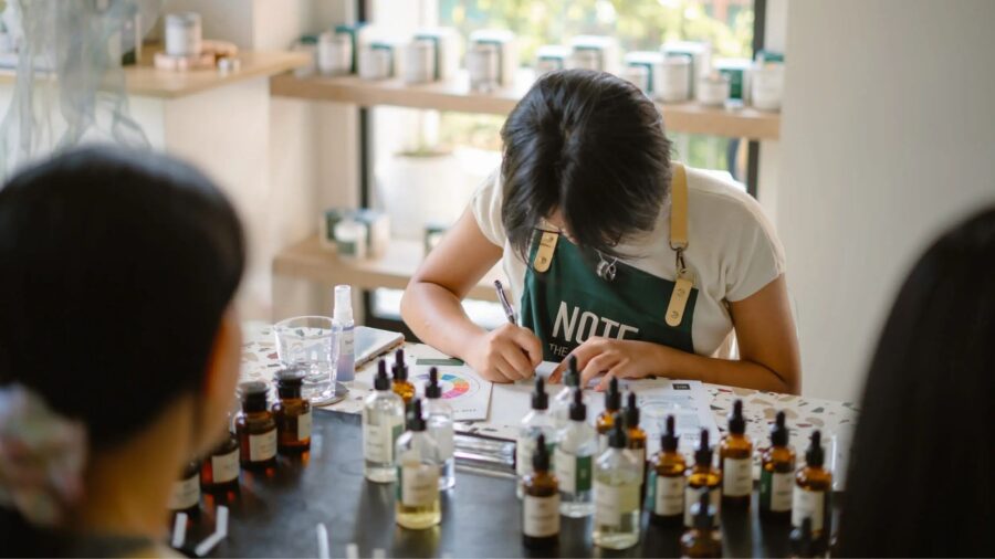 A participant writes down a fragrance formula during a perfume-making workshop, surrounded by essential oils and scent materials.
