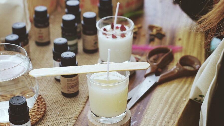 Handmade candles, fragrance oil bottles, and tools are arranged on a table during a candle-making workshop.