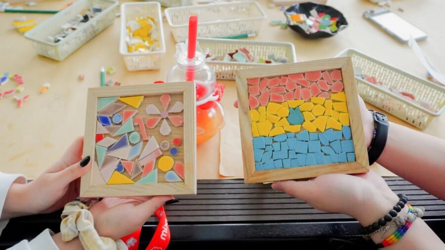 Two finished mosaic artworks with colorful tile patterns are held up at a craft workshop in Ho Chi Minh City.