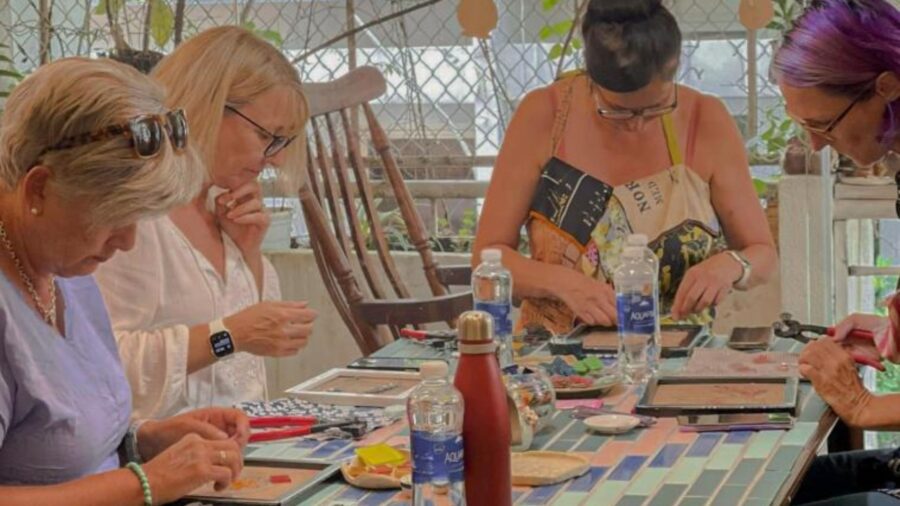 Participants work on mosaic art pieces at a workshop, arranging small colored tiles and materials into their chosen designs.