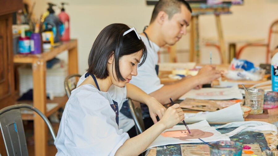 Travelers paint on canvas during a beginner-friendly painting workshop in Ho Chi Minh City, using brushes, paints, and prepared materials at a studio table.