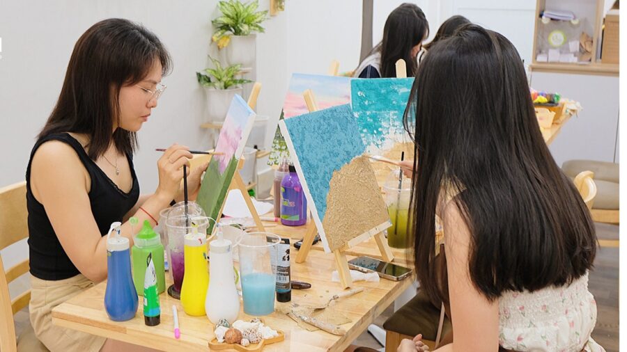 Participants sit around easels and paint colorful canvas artworks during a creative painting class in Ho Chi Minh City.
