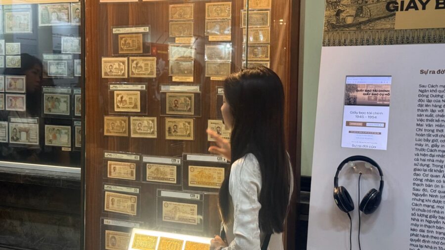 Visitor looking at financial notes and President Ho banknotes from 1945 to 1954 displayed in a glass case at the Vietnamese currency exhibition.