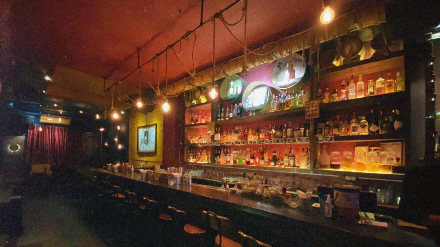 Interior view of Nê Cocktail Bar, a cozy cocktail bar in Hanoi with warm lighting, long counter, and colorful bottle display.